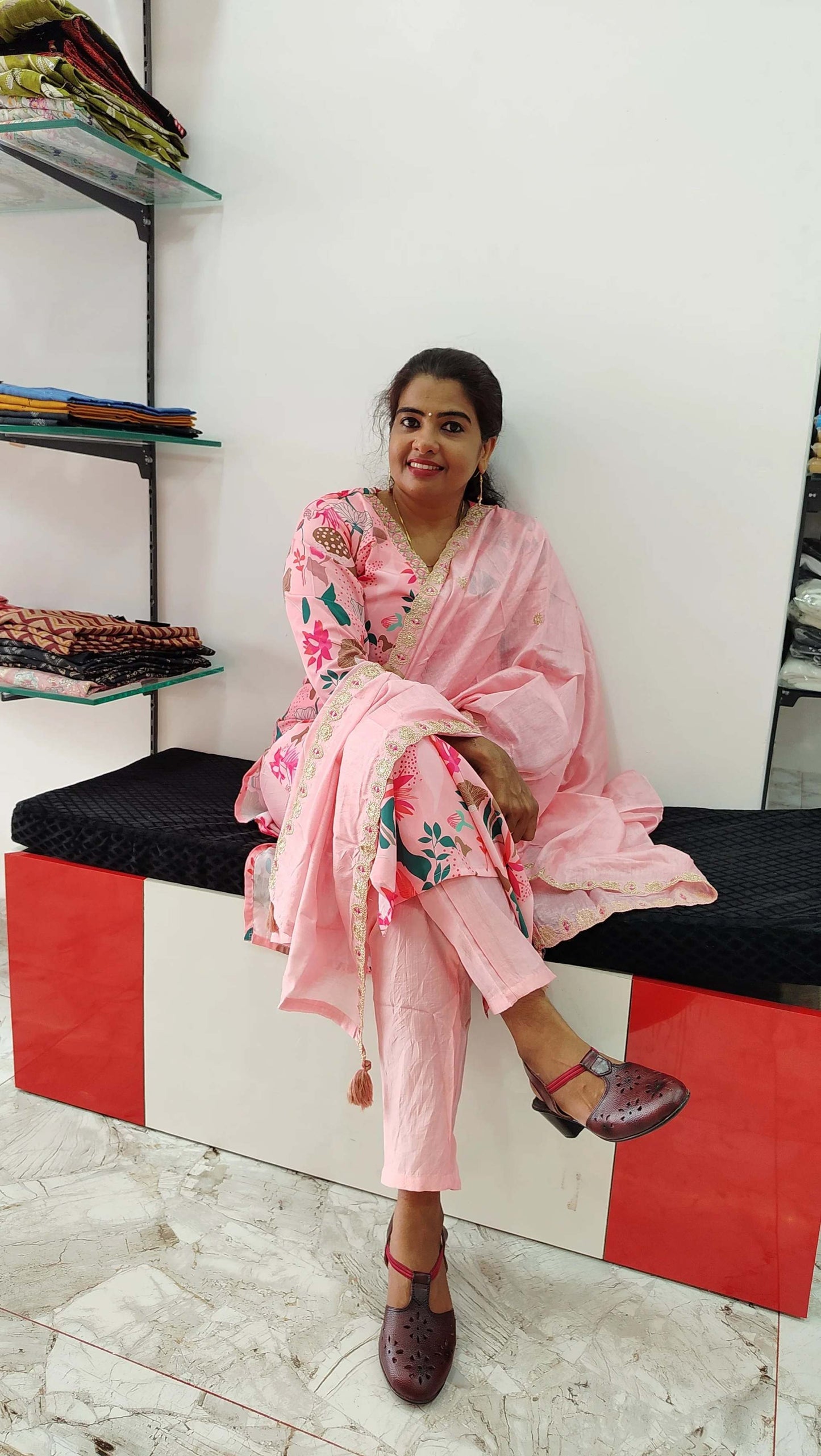 Woman wearing pink viscose maslin churidar set with floral print sitting on bench in fabric store