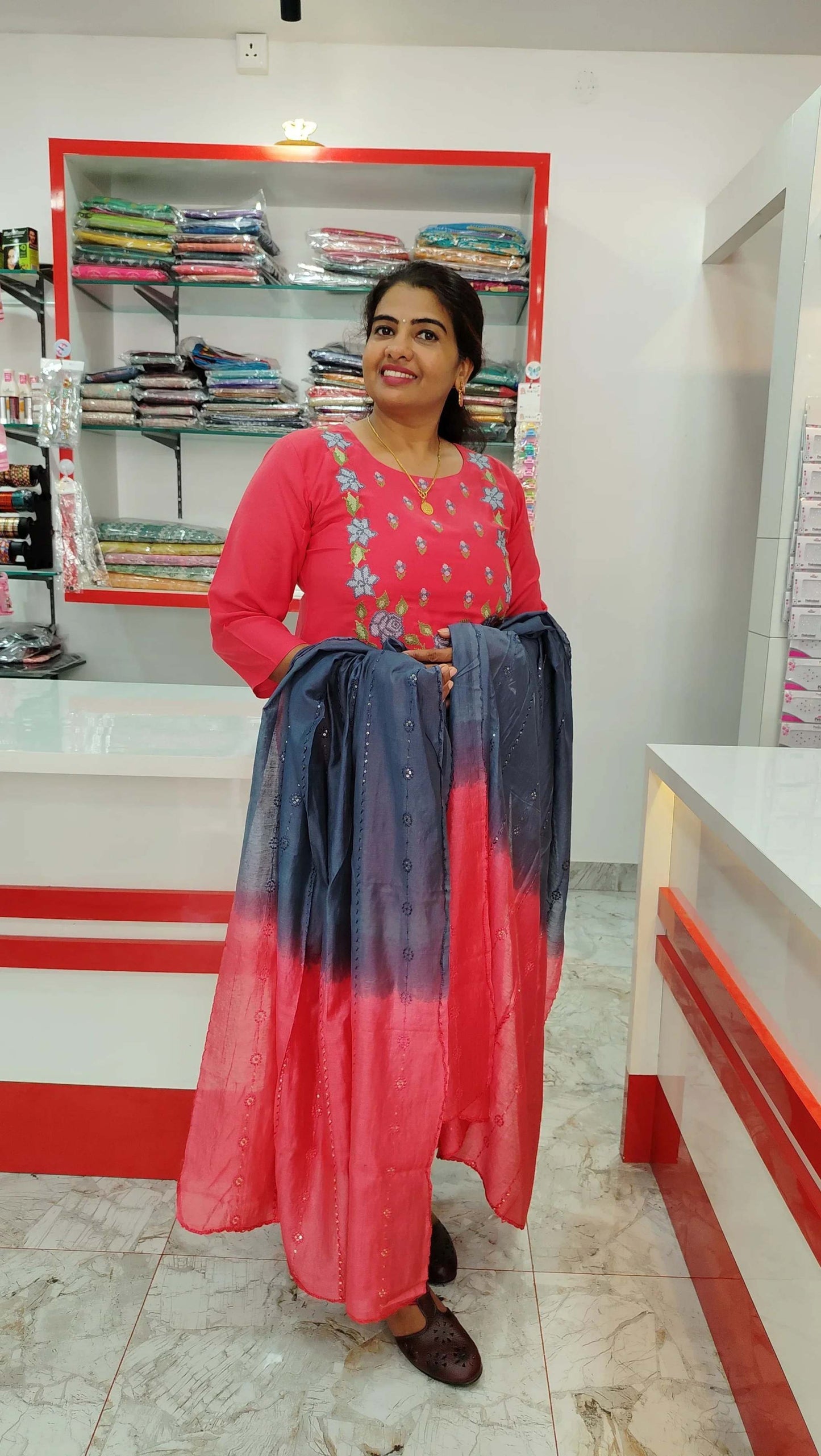 Woman wearing red embroidered churidar set holding matching dupatta in fabric store showroom