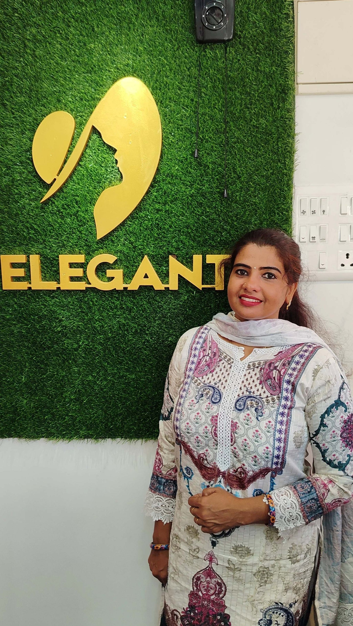Woman wearing a printed Kora Maslin churidar set standing in front of an Elegant store sign.