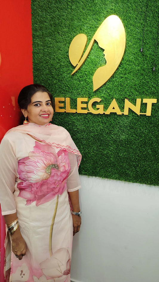 Woman wearing a pink floral Taby Silk churidar set standing in front of a green wall with Elegant brand logo