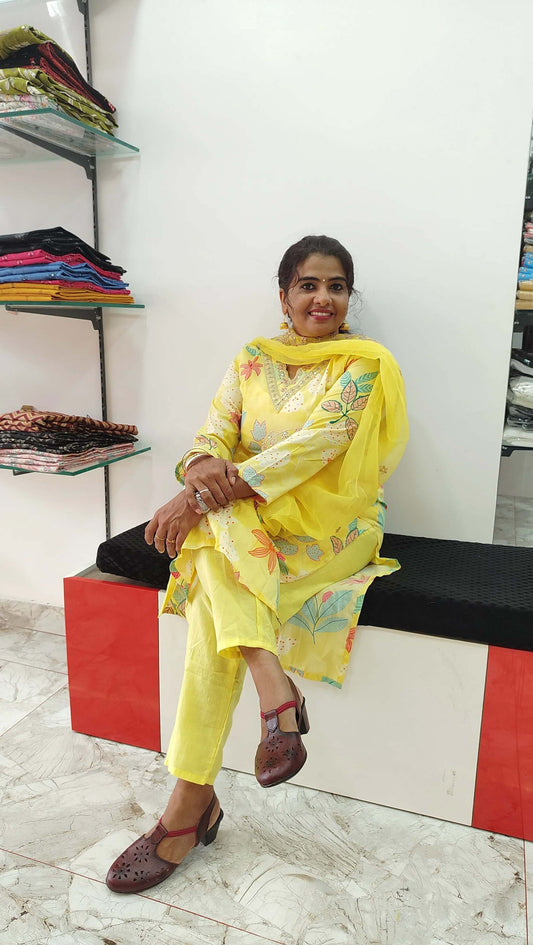 Woman wearing yellow silk churidar set with floral design sitting indoors