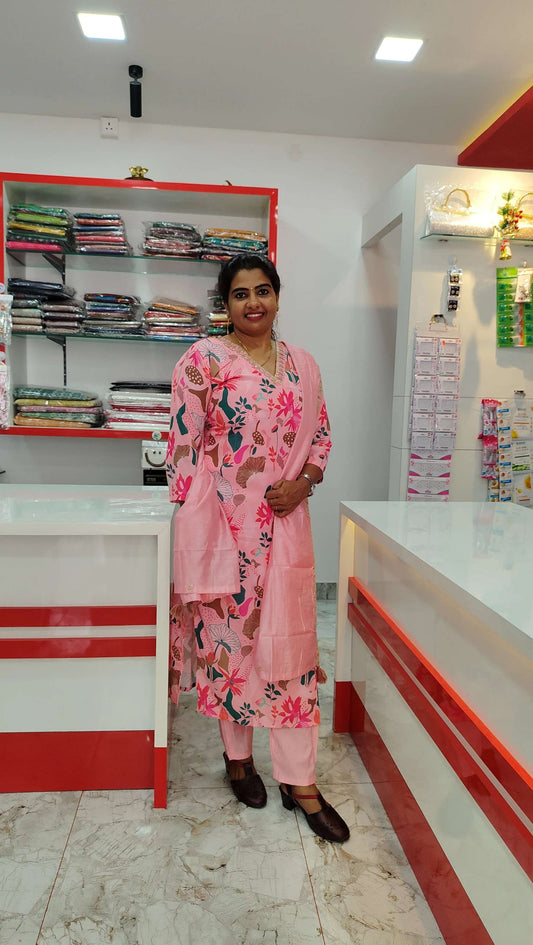 Woman wearing a pink floral churidar set standing in a clothing store with folded fabrics on shelves in the background