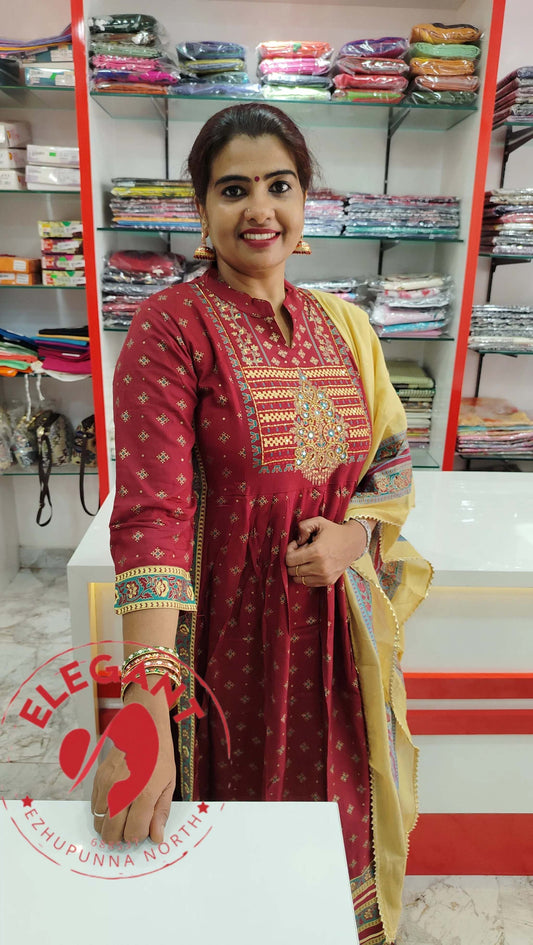 Woman wearing a red cotton churidar set with intricate embroidery and a yellow dupatta in a fabric store.