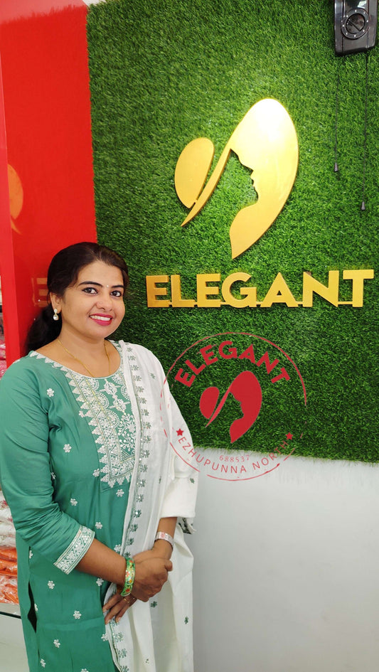 Elegant woman wearing green and white silk churidar set standing beside Elegant store logo on green wall background