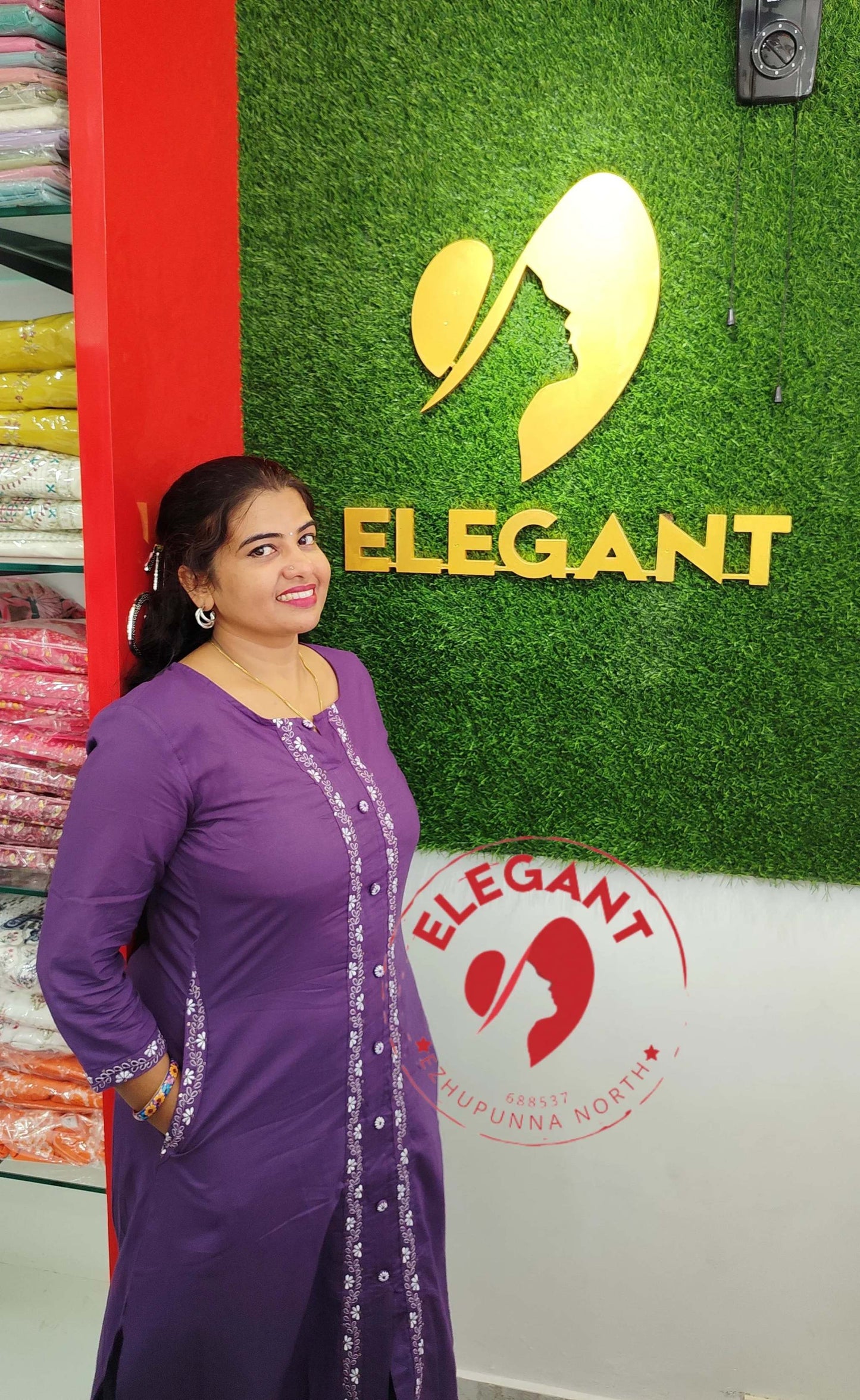 Woman wearing a purple Kurthi Set standing near a green wall with Elegant logo.