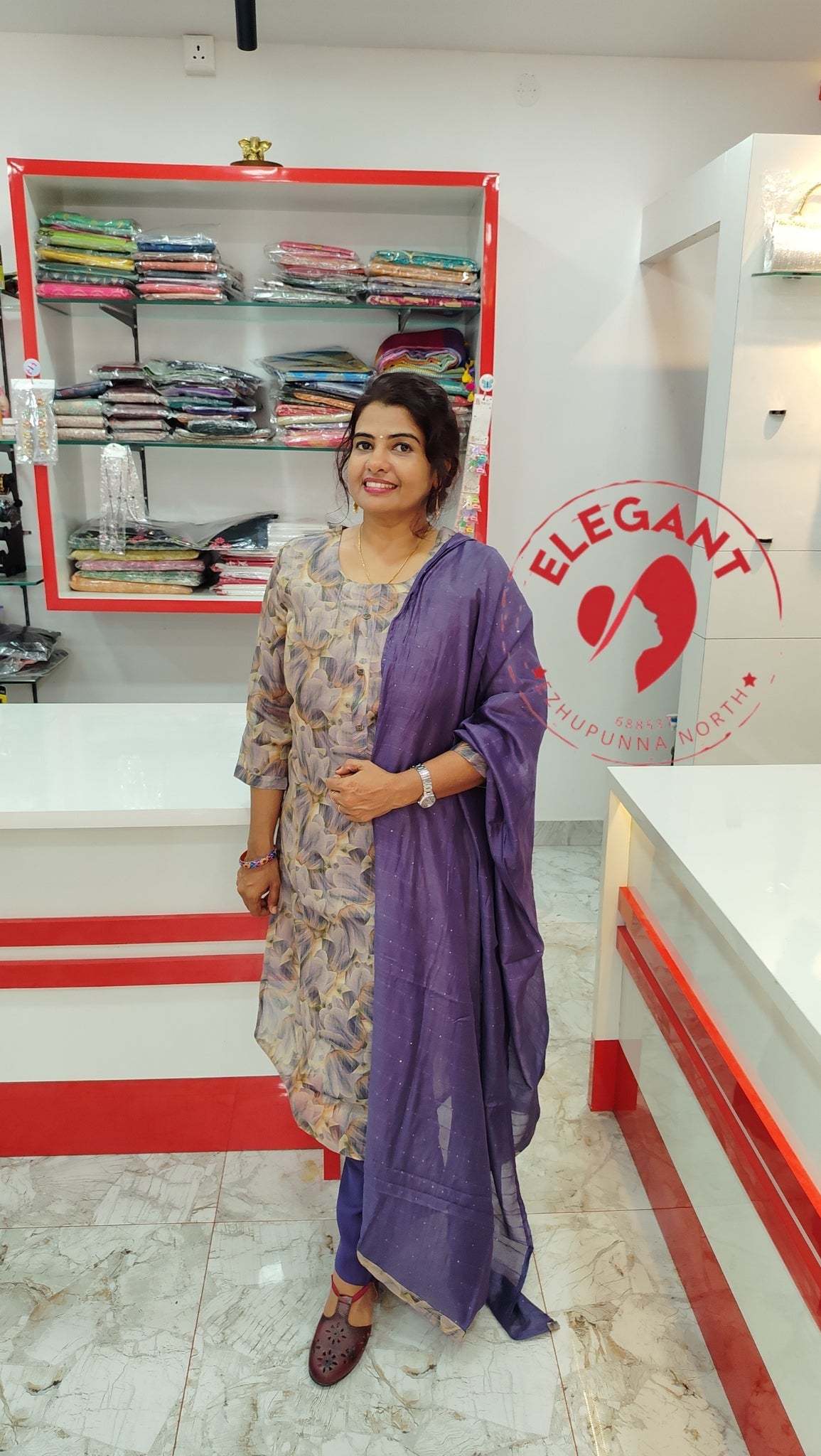 Woman wearing a shimmer fabric churidar set with purple dupatta, standing in a boutique showroom.