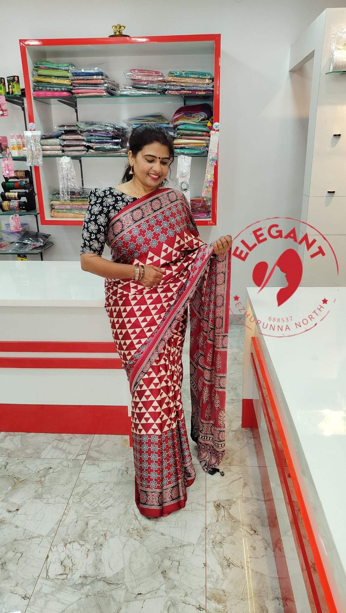 Woman wearing a red and white semi modal silk saree with geometric patterns in a fabric store showcasing Semi Modal Silk Sarees.
