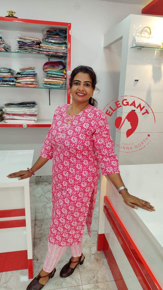 Woman wearing a pink and white floral printed Kurthi Set standing in a clothing store with shelves of folded clothes in the background