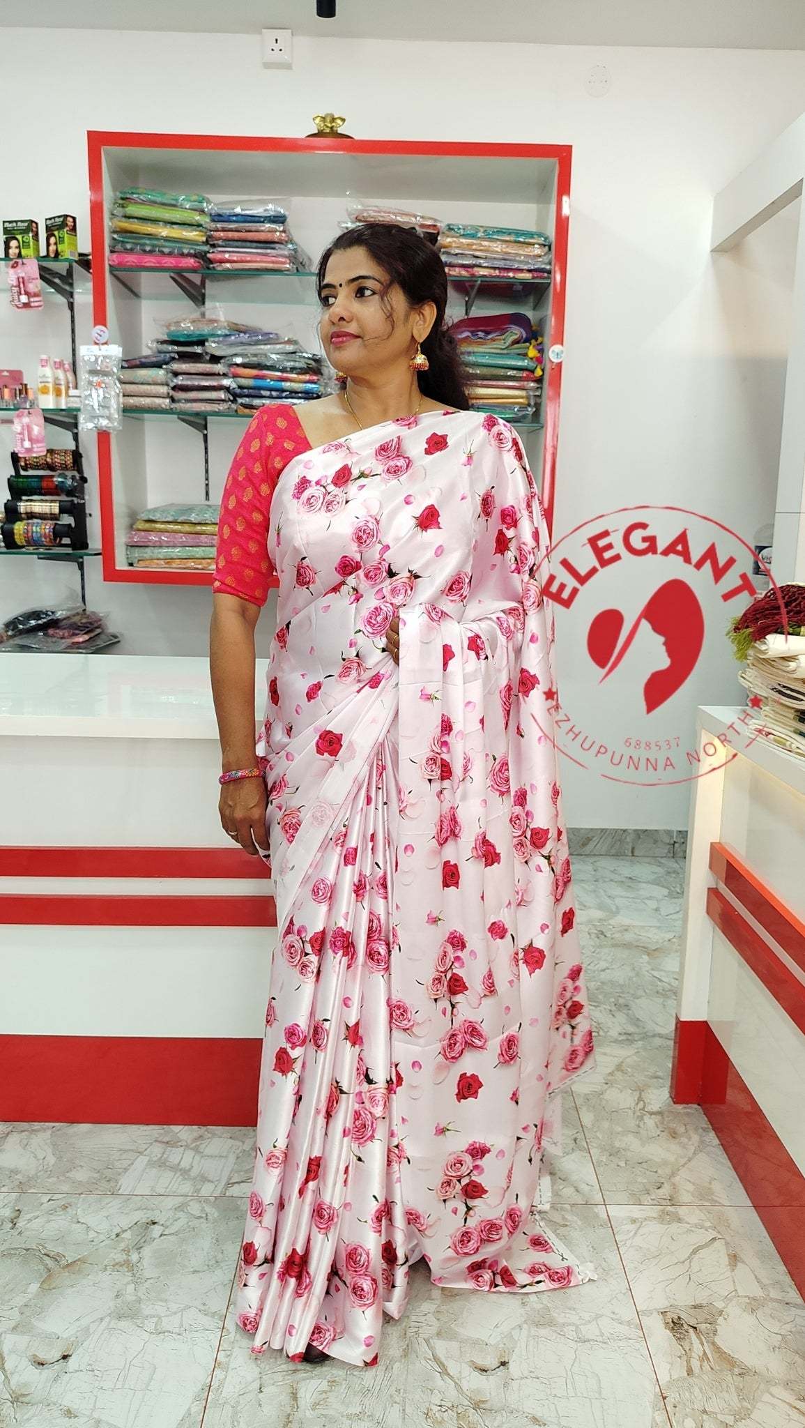 Woman wearing a white satin silk saree with red floral prints standing in a clothing store display.