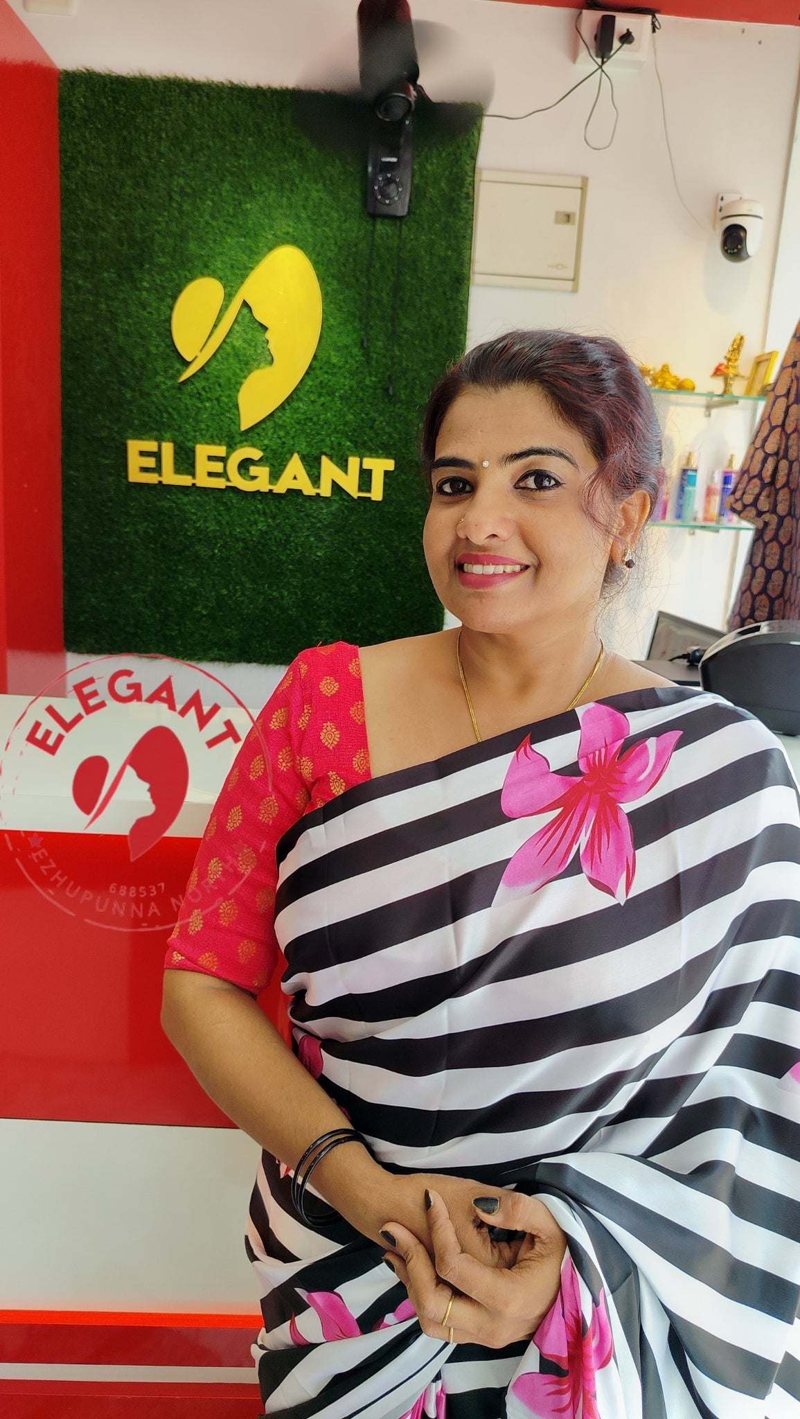 Woman wearing a black and white striped satin silk saree with pink floral design standing in Elegant store.
