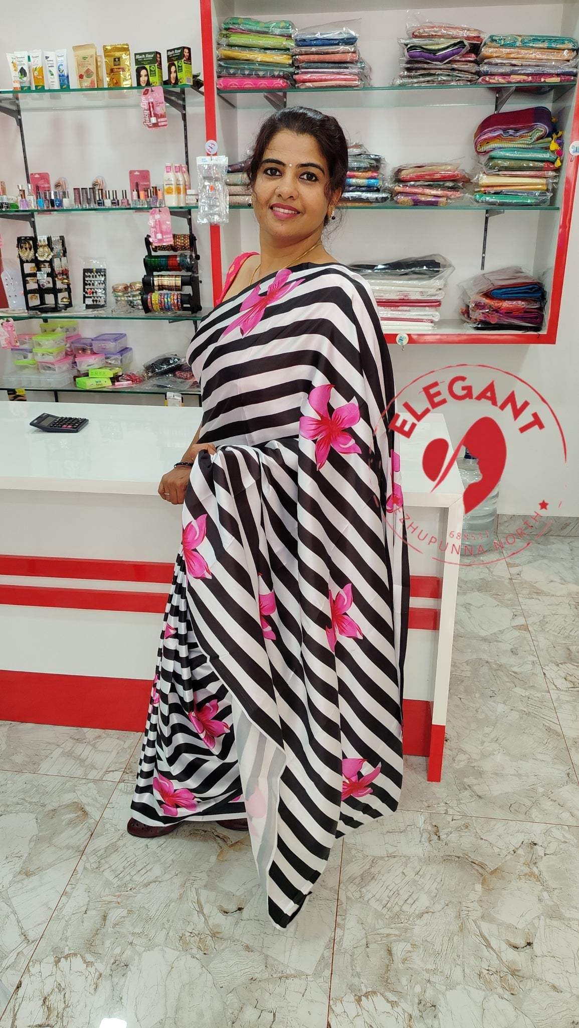 Woman wearing black and white striped satin silk saree with pink floral design in a fabric store showroom