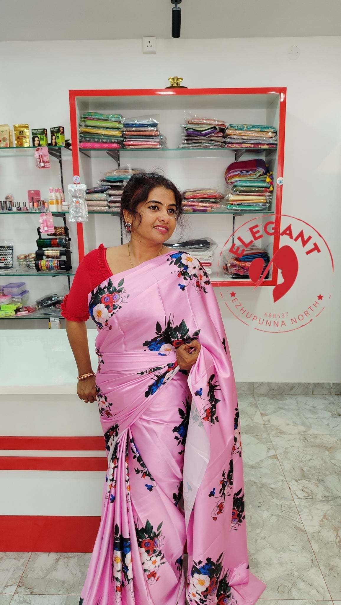 Woman wearing pink satin silk saree with floral print in a fabric store showcasing satin silk sarees for occasion and party wear