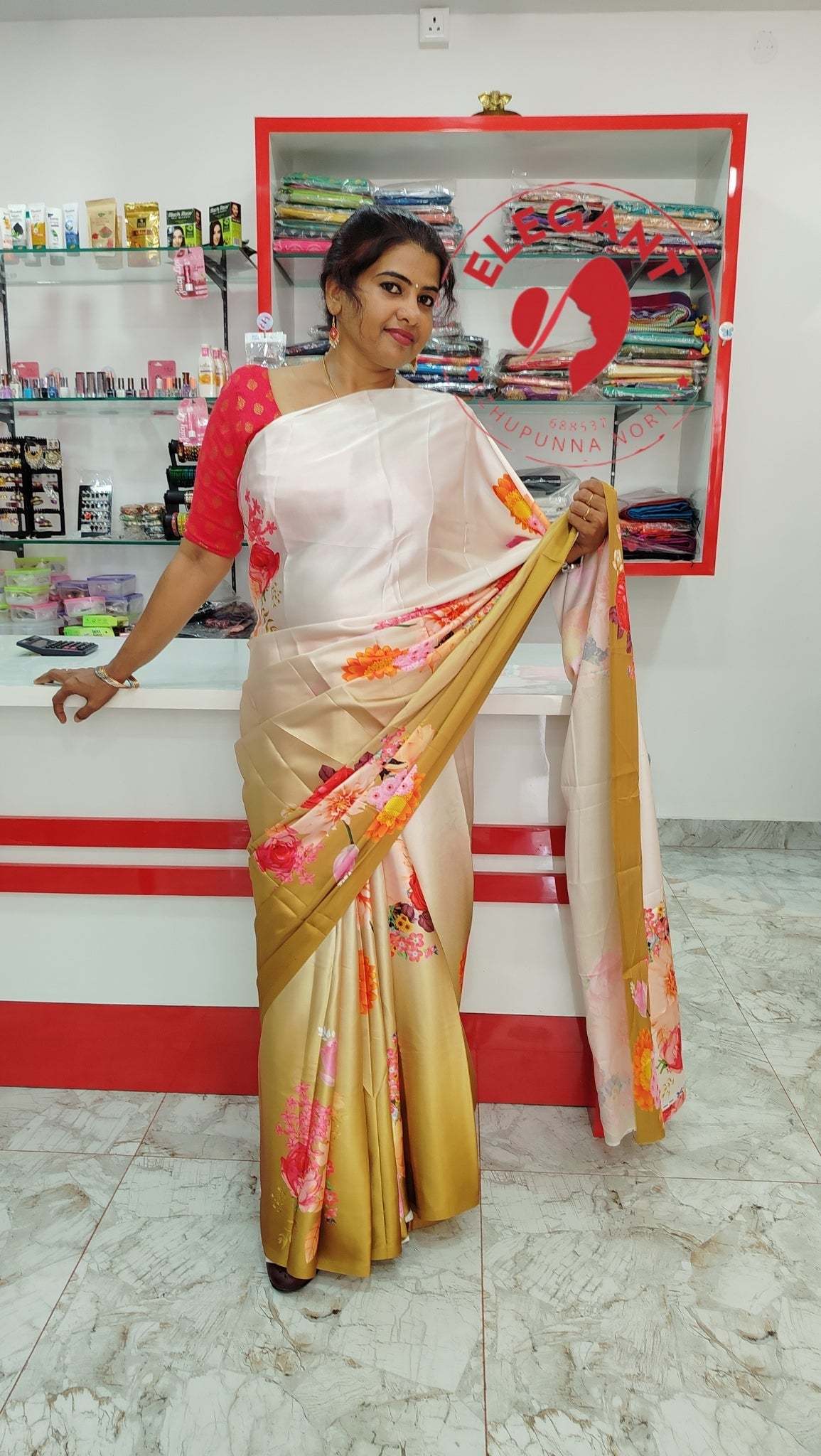 Woman wearing beige and white satin silk saree with red floral designs, posing in a store setting