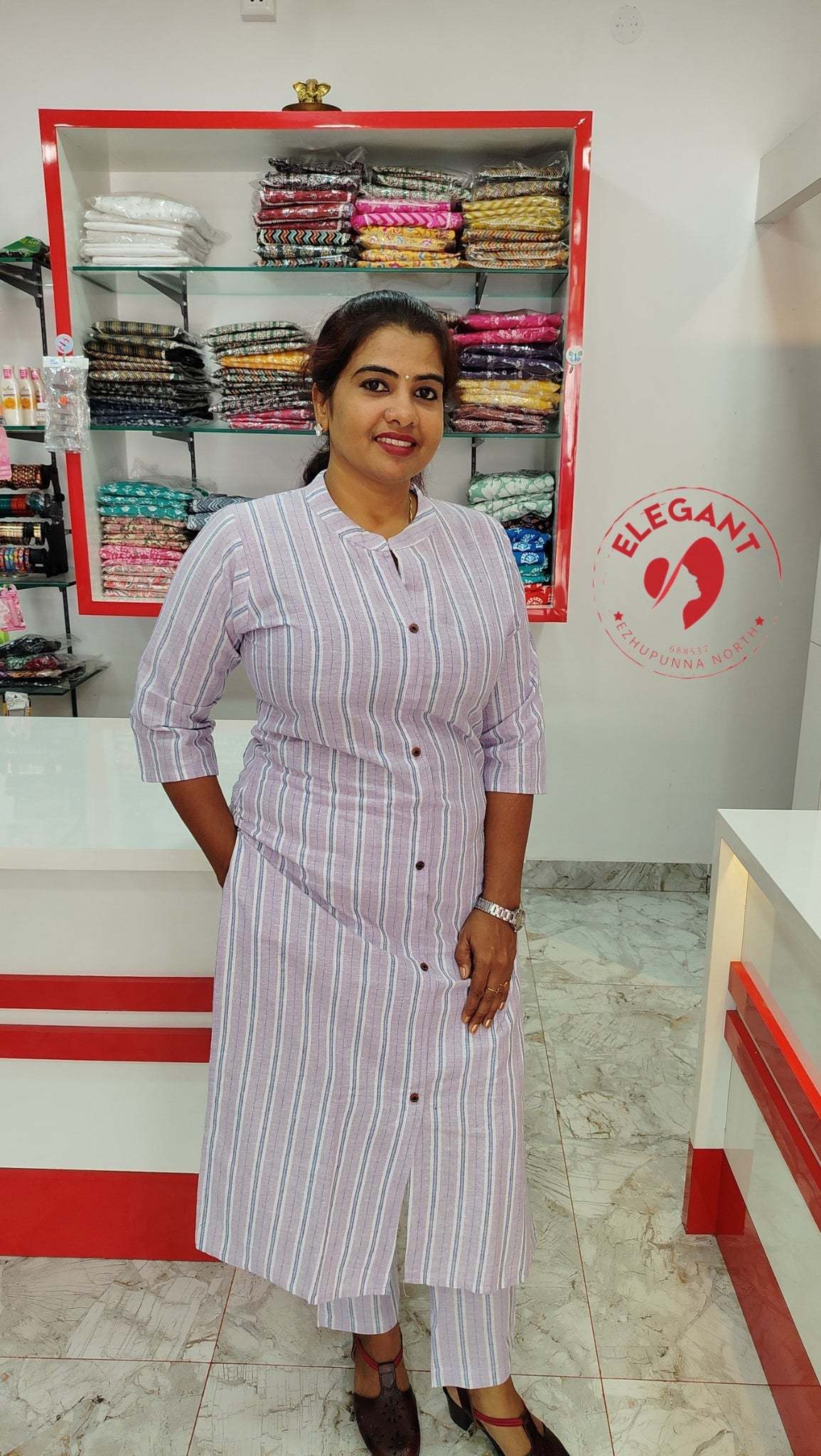 Woman wearing striped kurthi set standing in clothing store with shelves of folded fabric behind her