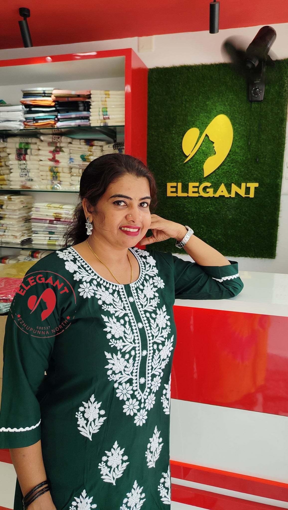 Woman wearing elegant green cotton top with white embroidery standing in clothing store