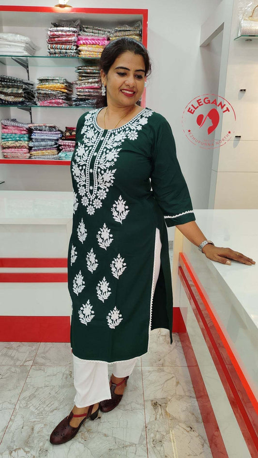 Woman wearing a green cotton top with white floral embroidery, standing in a clothing store.