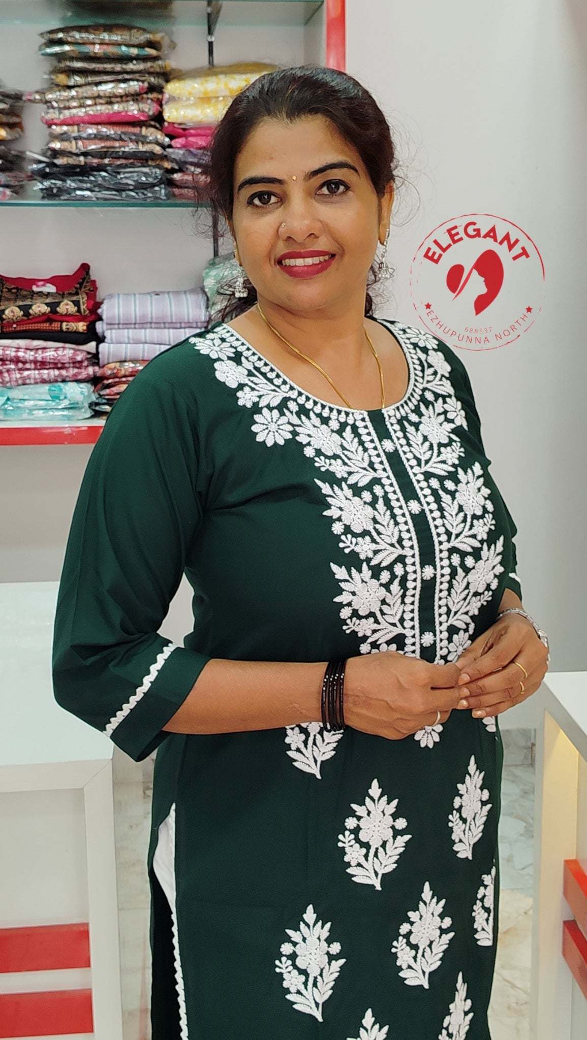 Woman wearing a green cotton top with white floral embroidery, standing in a clothing store.