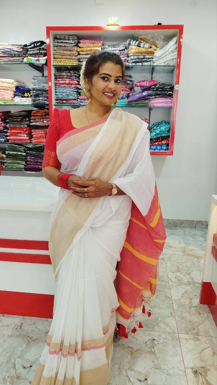 Woman wearing mul cotton set saree with kasavu border and rich red pallu with tassels in a textile store