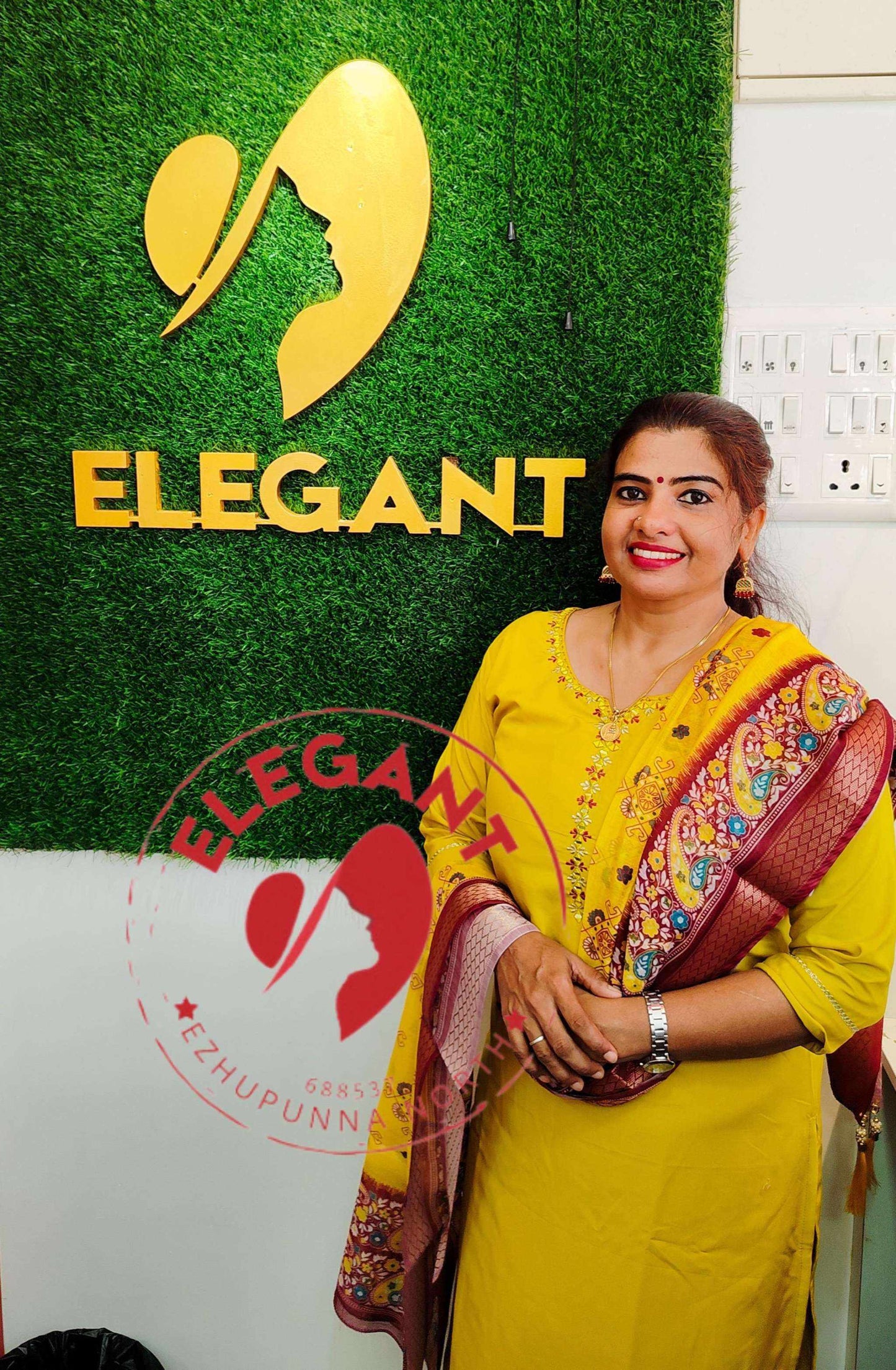 Woman wearing yellow Roman silk churidar with patterned silk dupatta standing in front of Elegant store sign