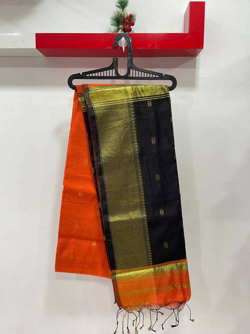 Saree with orange, green, and black patterns hanging on a red shelf.