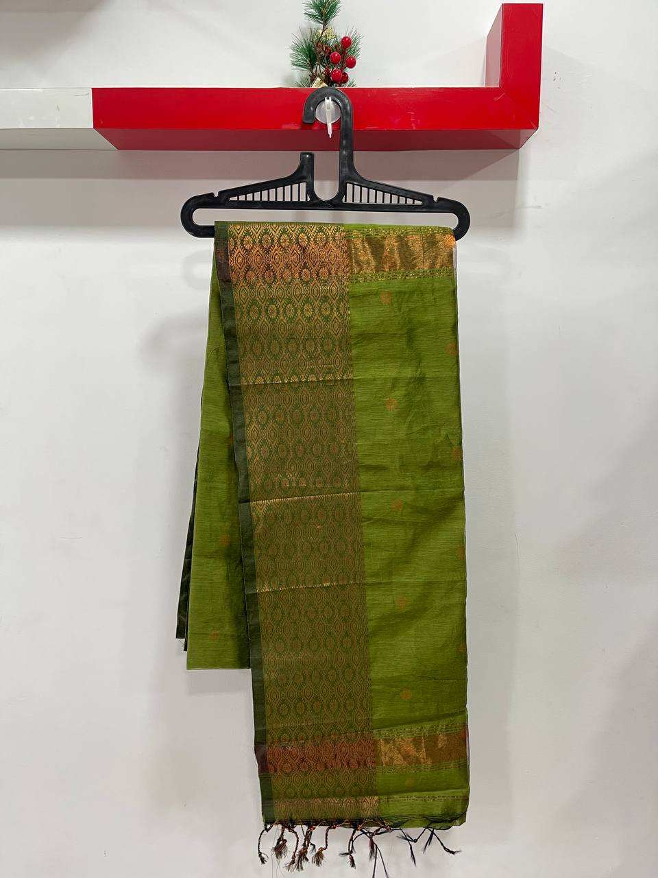 Green saree with brown patterns hanging on a black hanger against a white wall.