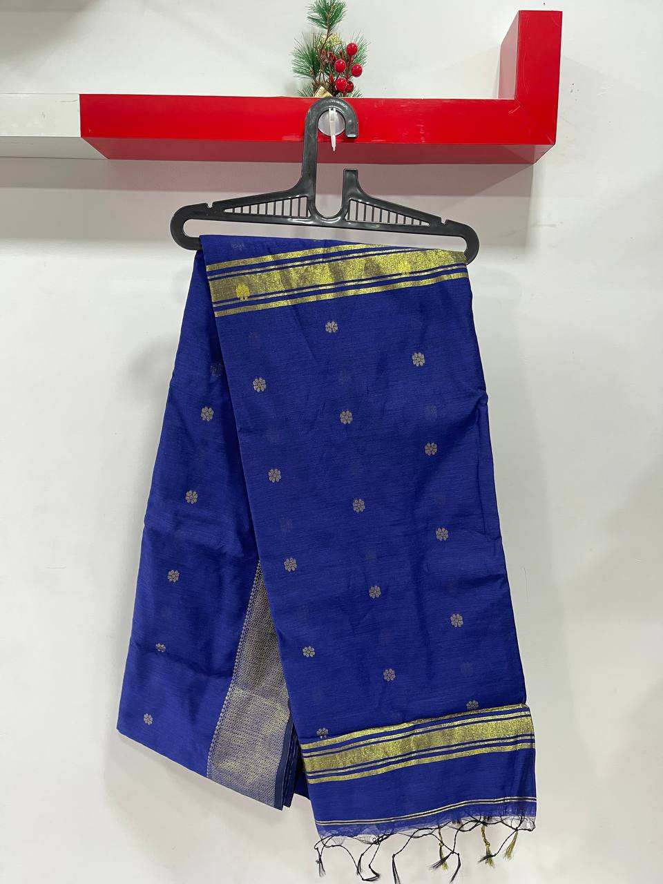 Blue saree with gold border on a hanger against a white wall.