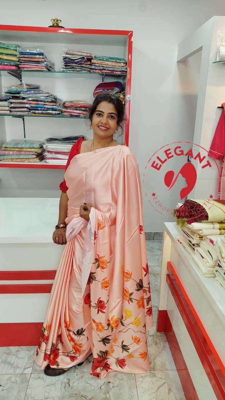 Woman wearing a peach satin silk saree with floral print standing in a fabric store showcasing elegant satin silk sarees for occasion and party wear.