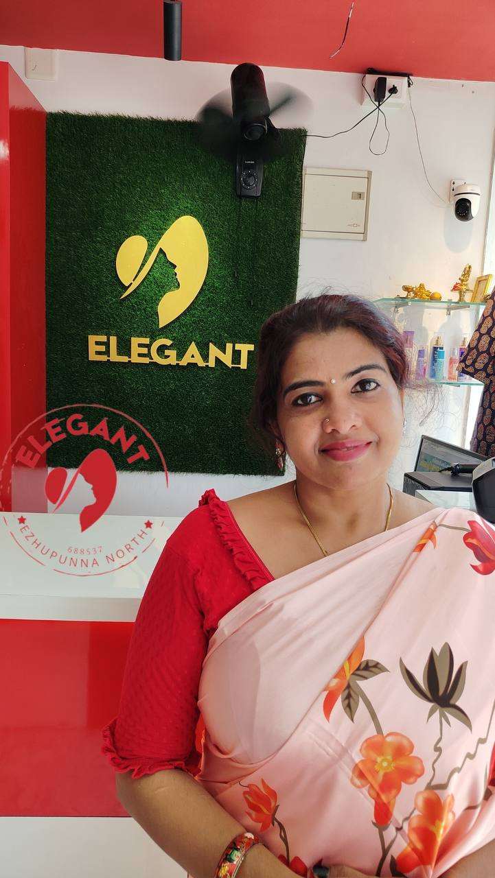 Woman wearing a floral satin silk saree in a store with Elegant brand signage in the background.