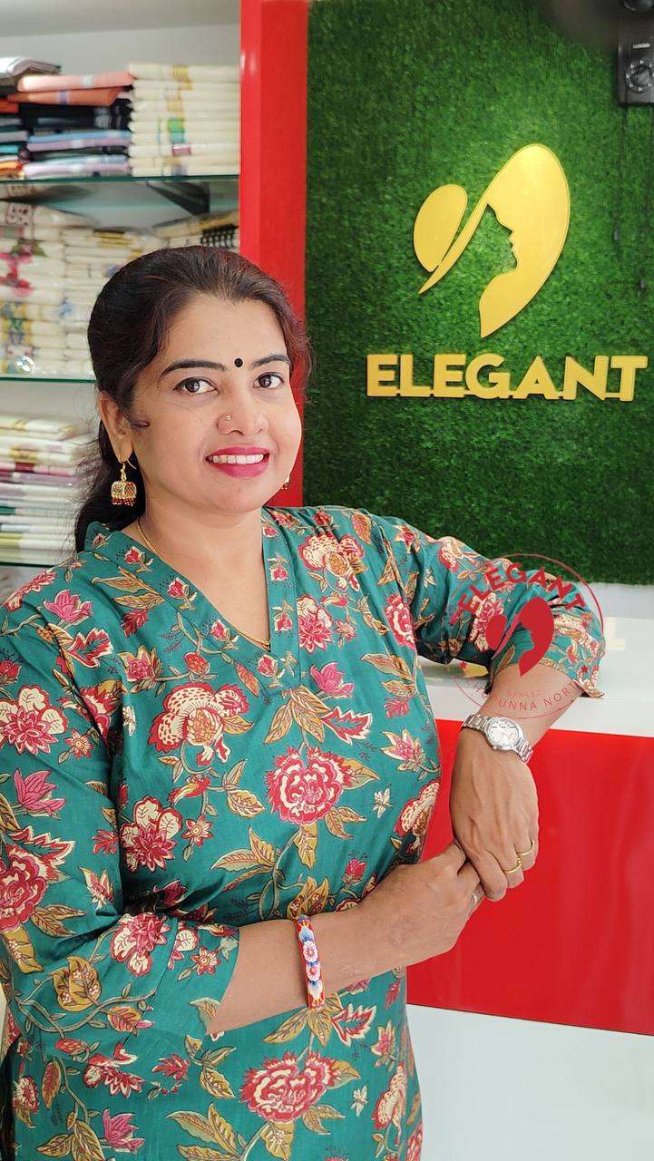 Woman wearing a vibrant floral Kurthi Set made of high-quality cambric cotton standing near Elegant store sign