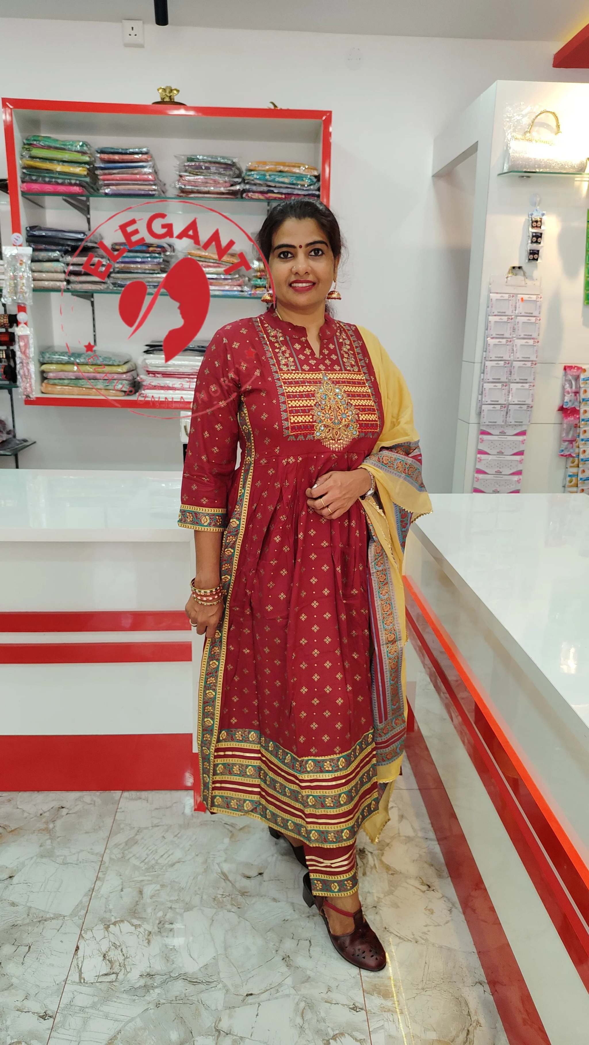 Woman wearing a maroon and mustard cotton churidar set with traditional prints, standing in a boutique.