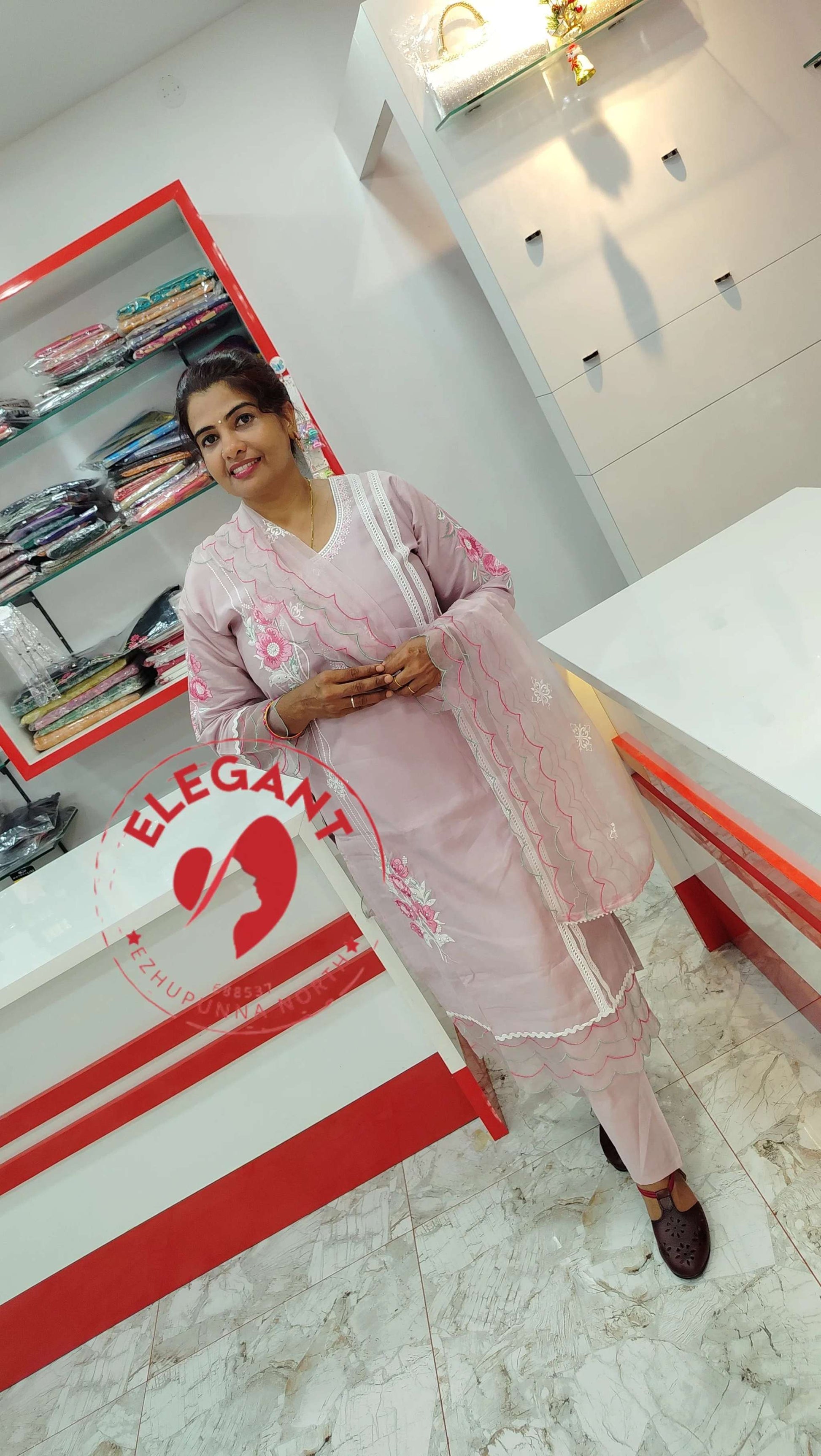 Woman wearing a pink silk churidar set with floral embroidery standing in a modern clothing store.