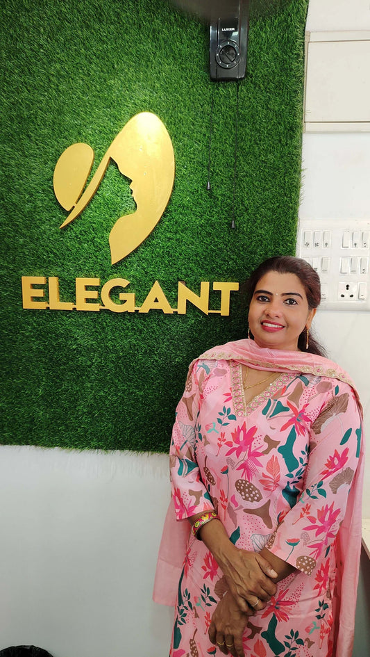 Woman wearing pink floral churidar set standing in front of a green wall with "ELEGANT" logo.