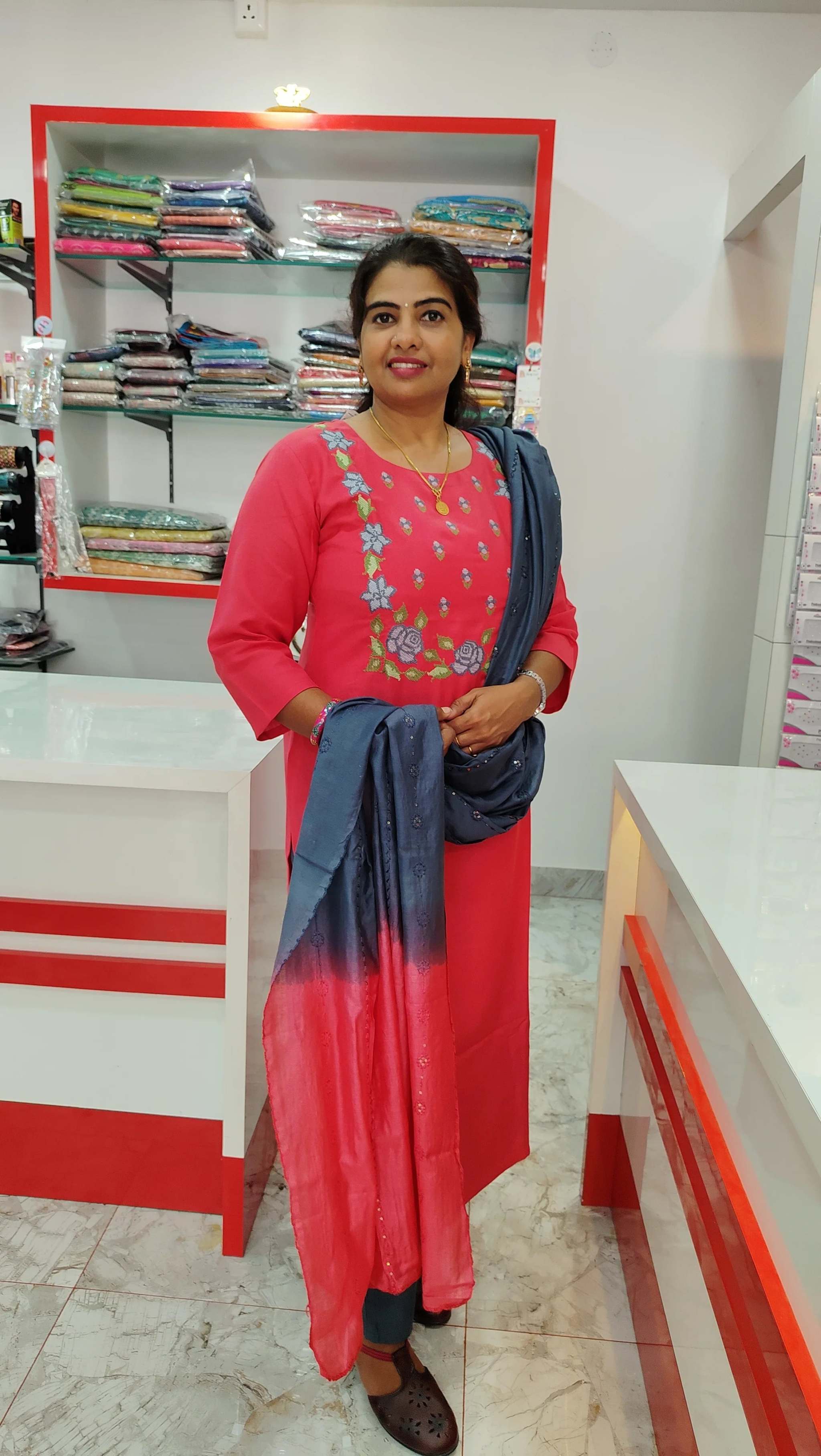 Woman wearing a pink cotton churidar set with blue dupatta, standing in a clothing store showroom