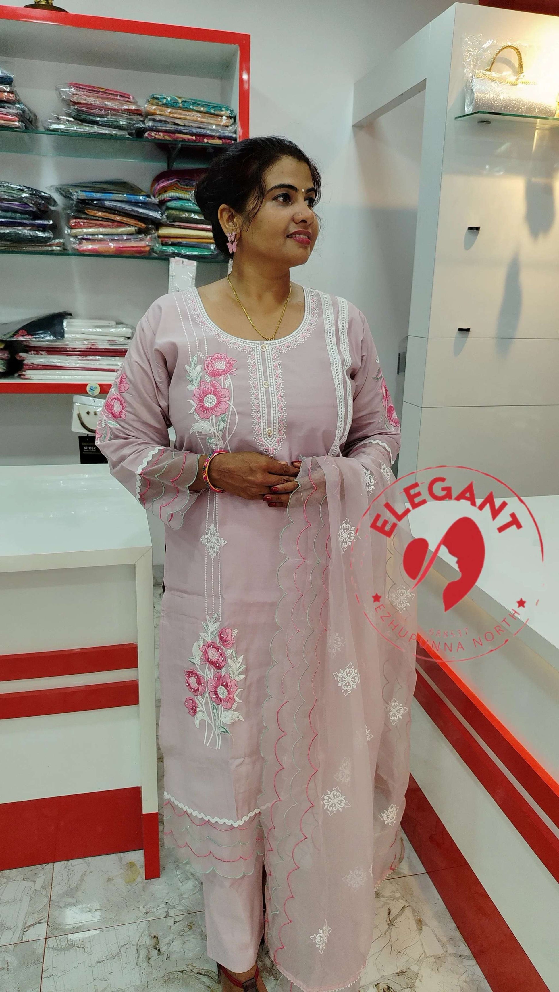 Woman wearing pink silk churidar set with floral embroidery standing in a boutique showroom
