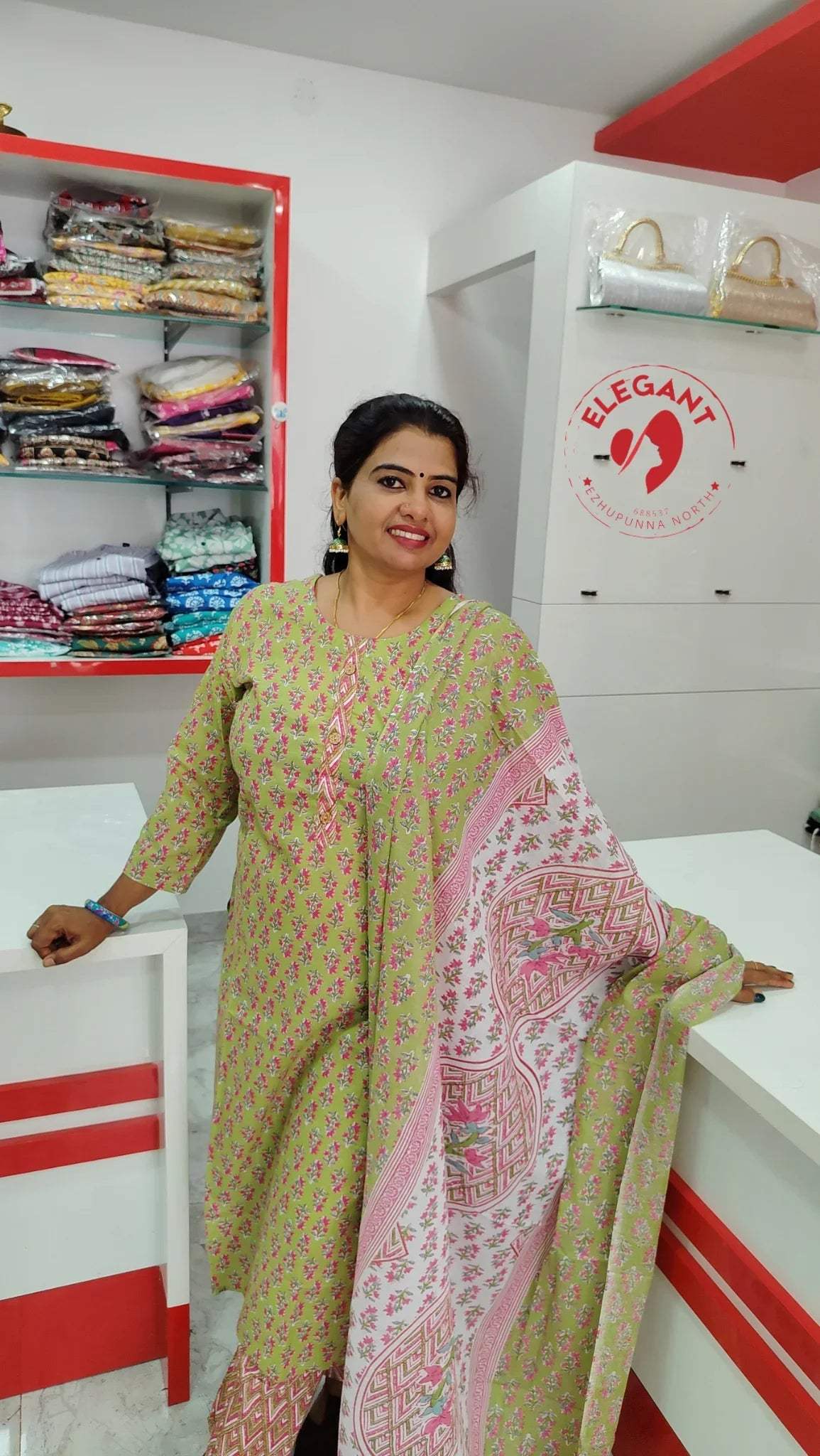 Woman wearing a green cotton churidar set with pink floral print and matching pink patterned dupatta in a clothing store setting