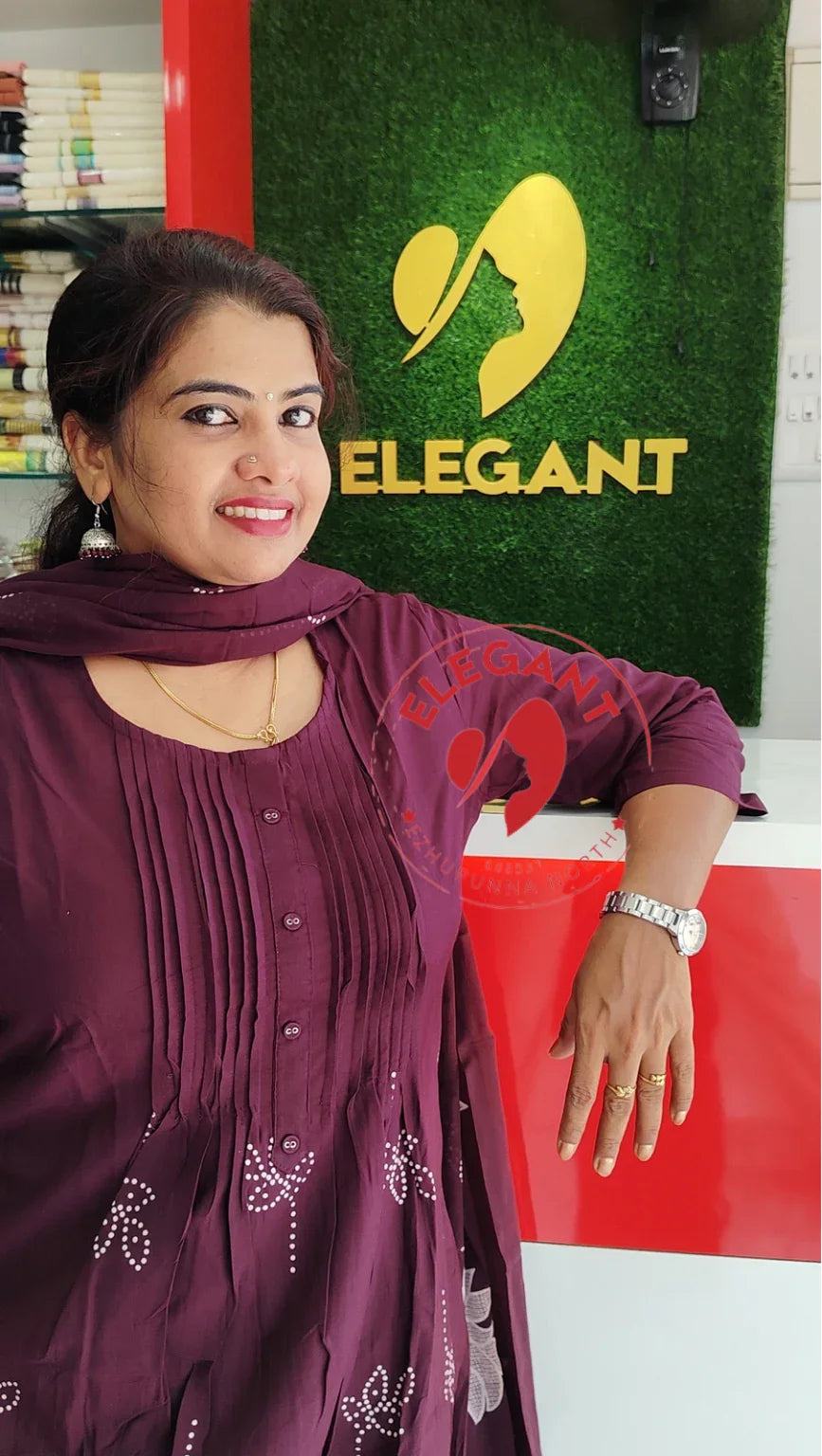 Woman wearing a maroon mul mul cotton churidar set standing by a red and green Elegant Style Sanctuary sign