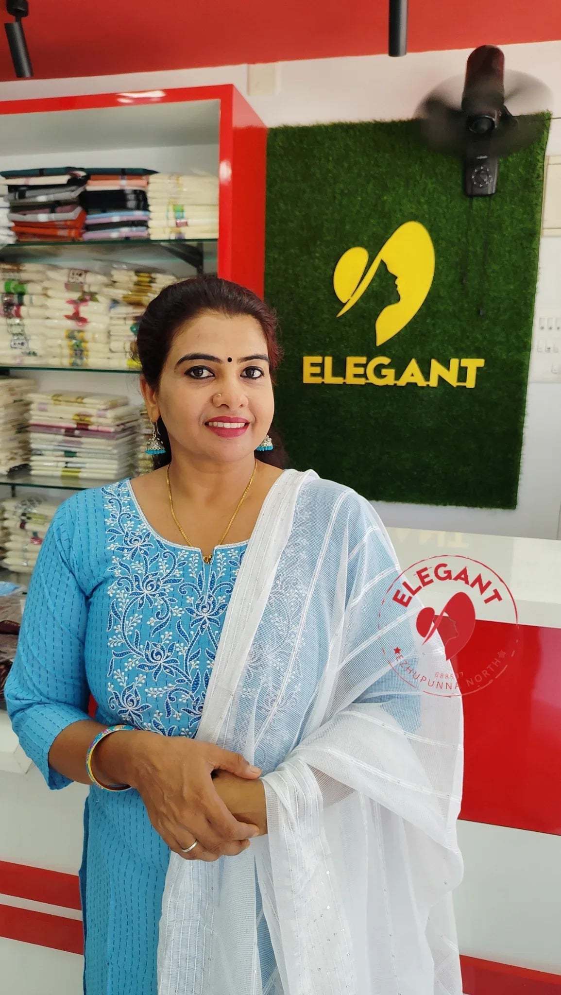 Woman in blue silk churidar set with white dupatta standing inside Elegant store