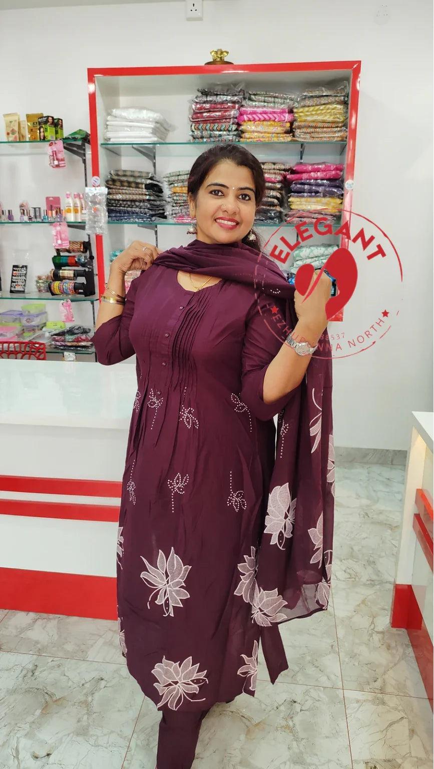 Woman wearing a maroon mul mul cotton churidar set with white floral prints in a clothing store.