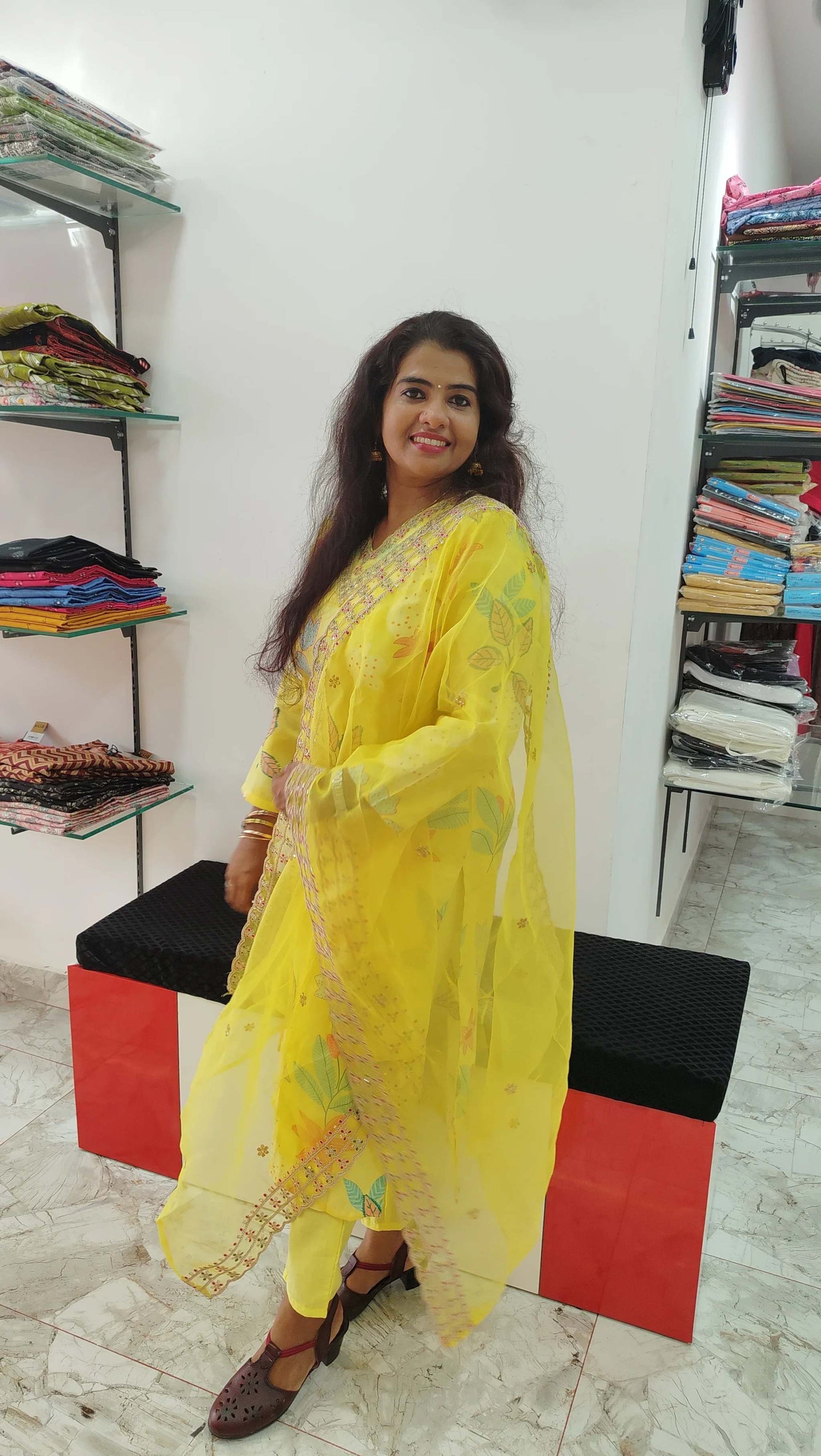 Woman wearing a yellow silk churidar set with floral patterns in a fabric store