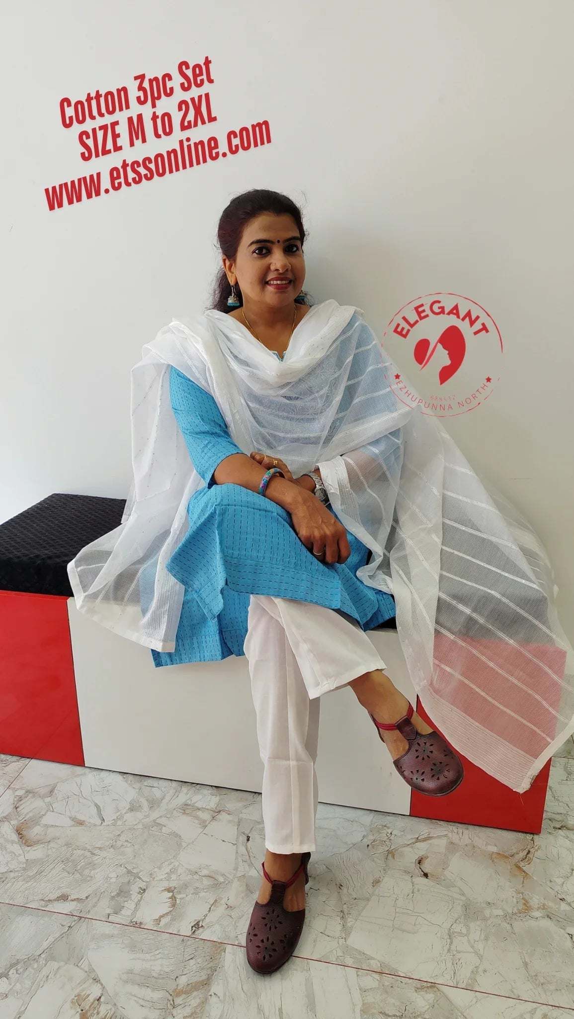 Blue silk churidar set with white dupatta and white churidar trousers worn by seated woman indoors