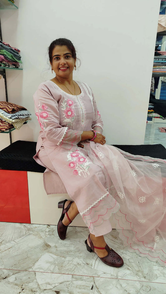 Woman wearing a pink silk churidar set with floral embroidery sitting in a store.