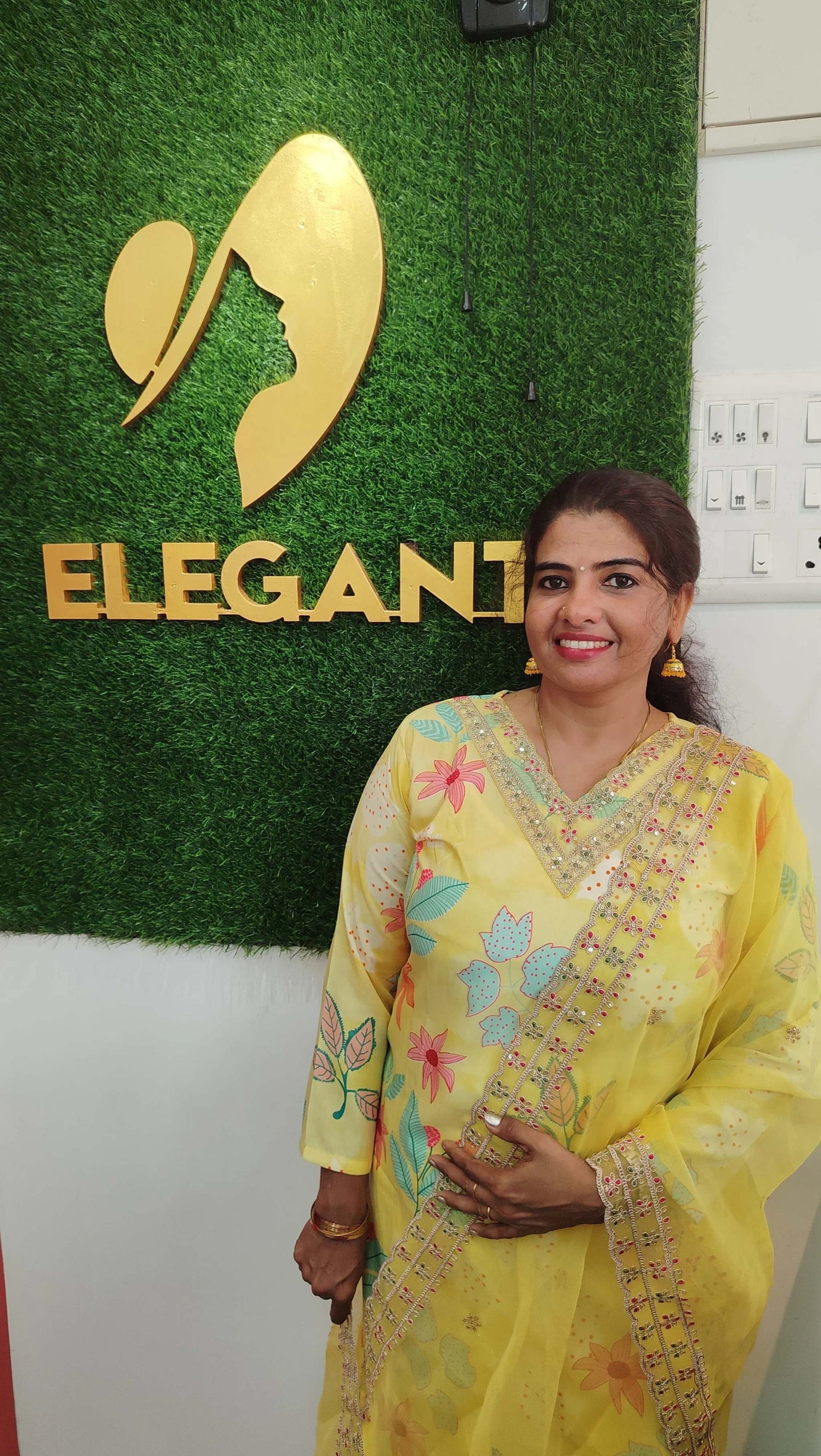 woman wearing yellow silk churidar set standing indoors near green wall with elegant logo