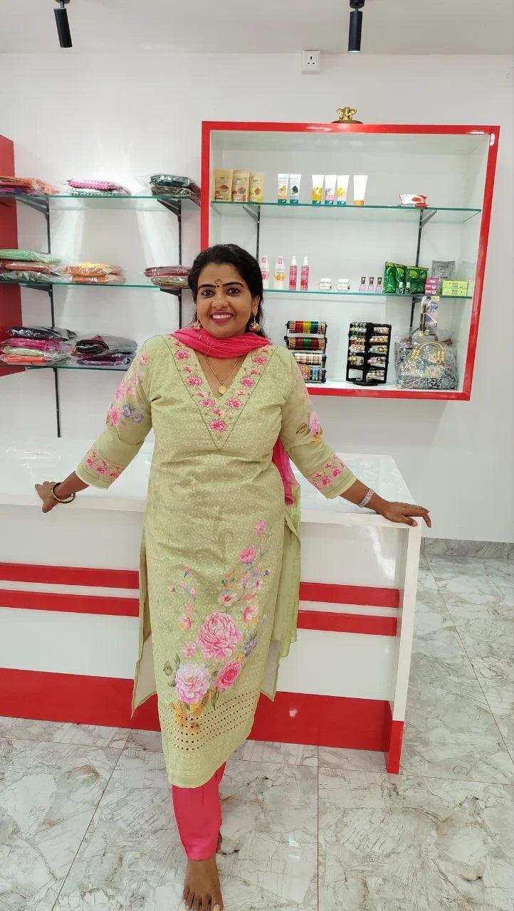 Woman wearing beige cotton churidar set with pink floral embroidery and pink dupatta standing in a store interior