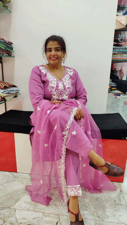 Woman wearing pink silk churidar set with white embroidery sitting on a bench in a fabric store
