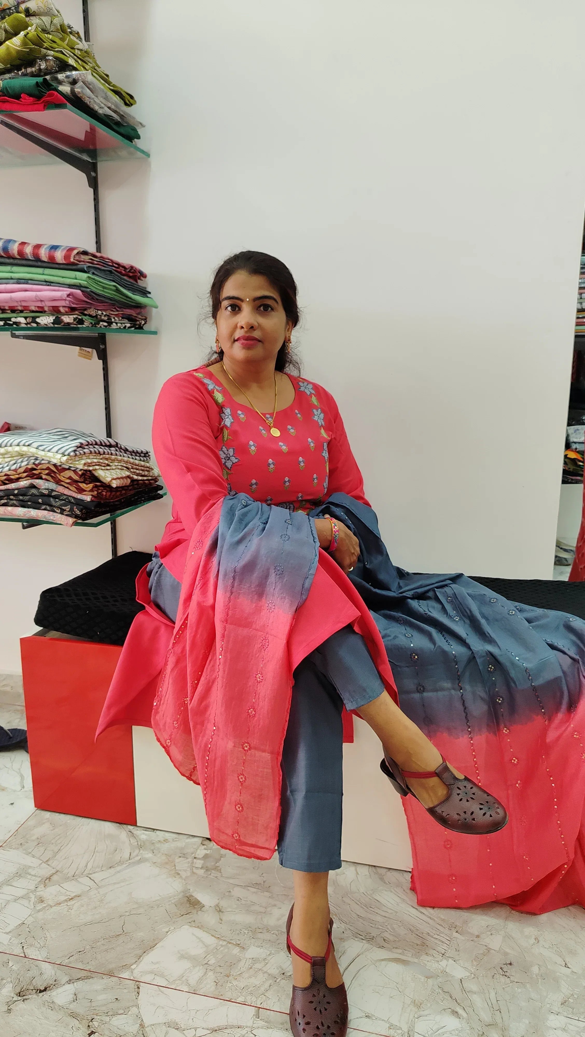Woman wearing pink and blue cotton churidar set sitting indoors near fabric shelves