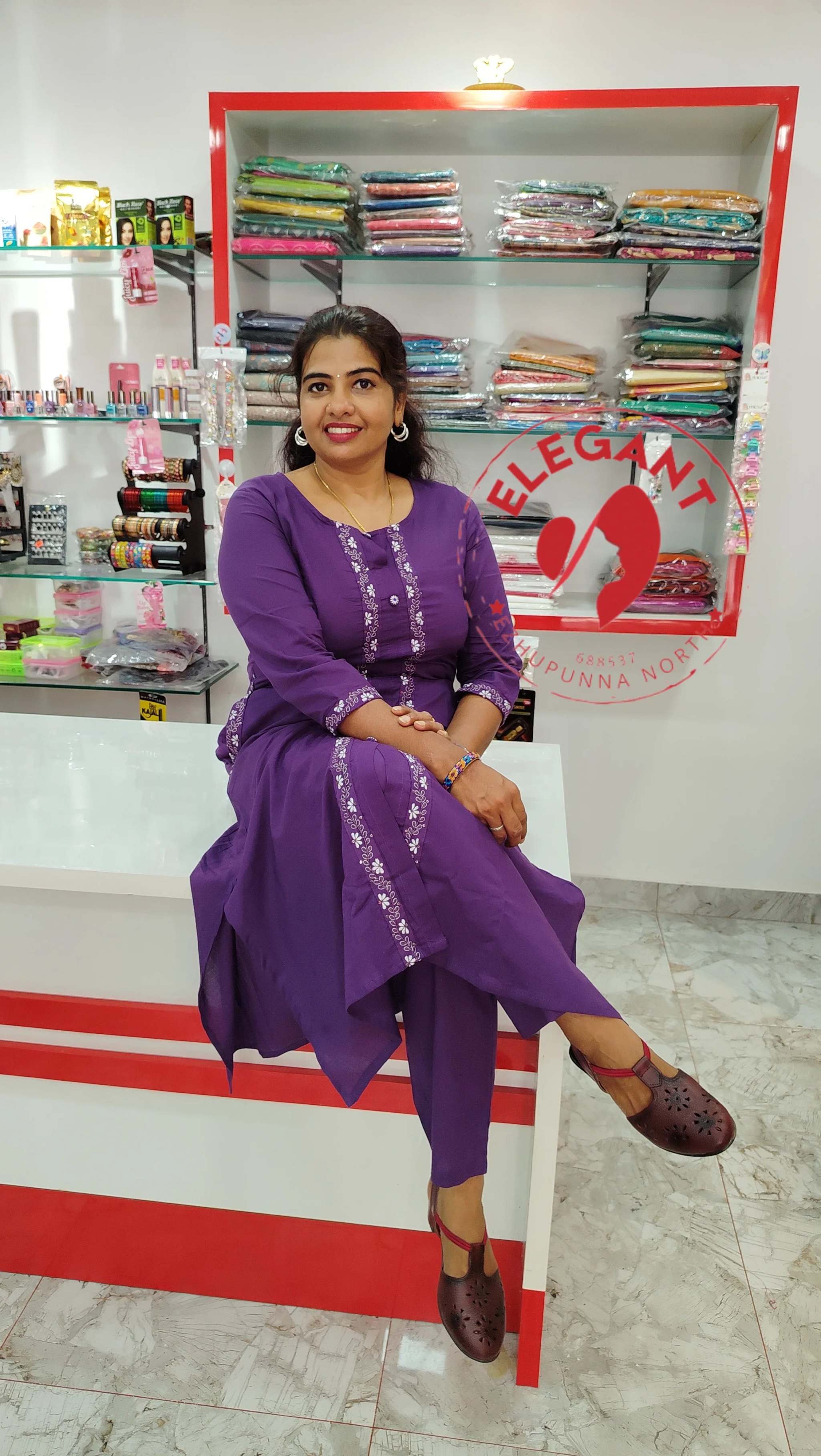 Woman wearing purple cotton Kurthi Set sitting in a clothing store with folded fabric in the background