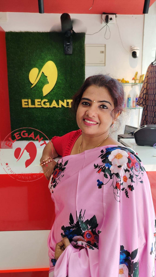 Woman wearing a pink satin silk saree with floral print posing indoors at Elegant – The Style Sanctuary store.