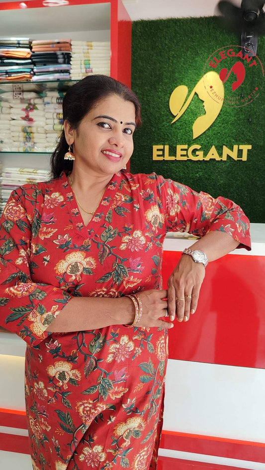Woman wearing a red floral Kurthi Set standing in a clothing store with folded fabrics in the background