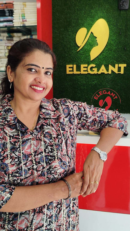 Woman wearing an imported crepe top with floral pattern standing by Elegant brand signage