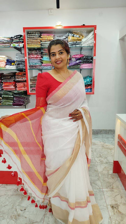 Woman wearing a white mul cotton saree with a kasavu border and rich red pallu with tassels in a fabric store